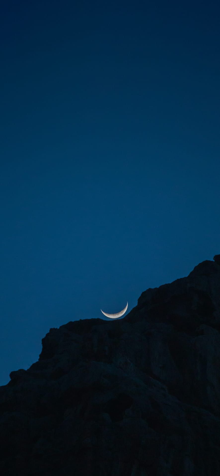 Crescent moon rising above rocky cliffs in Sa Calobra, Spain at twilight, ideal for Phone Wallpaper.