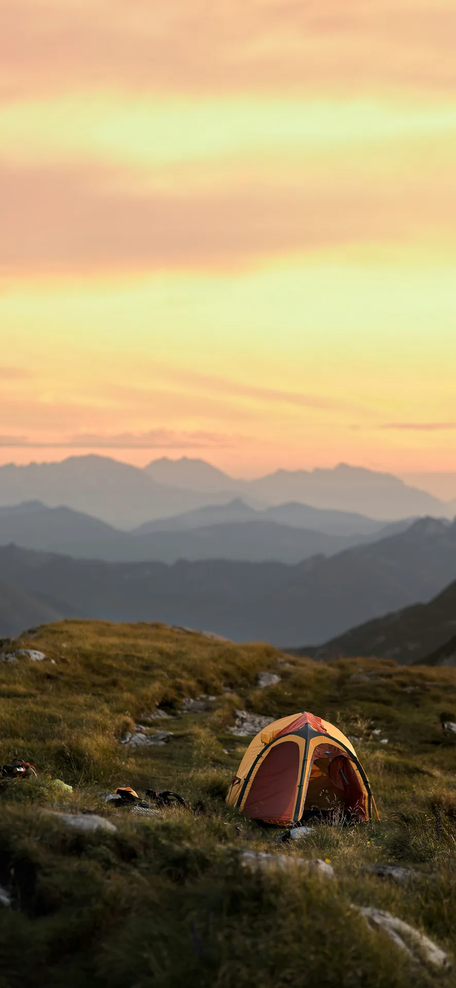 Colorful tent on grassy mountain ridge at sunset in Salzkammergut, Austria, surrounded by misty alpine layers—ideal nature Phone Wallpaper.