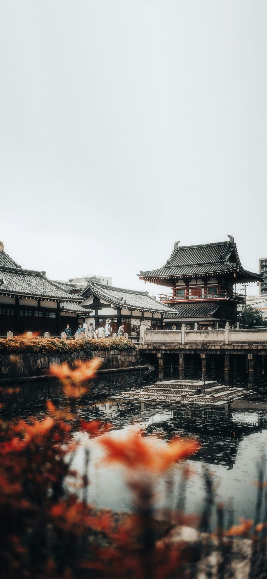 Traditional Japanese temple reflected in a calm pond with people nearby and soft autumn foliage, perfect for cultural landmark Phone Wallpaper.